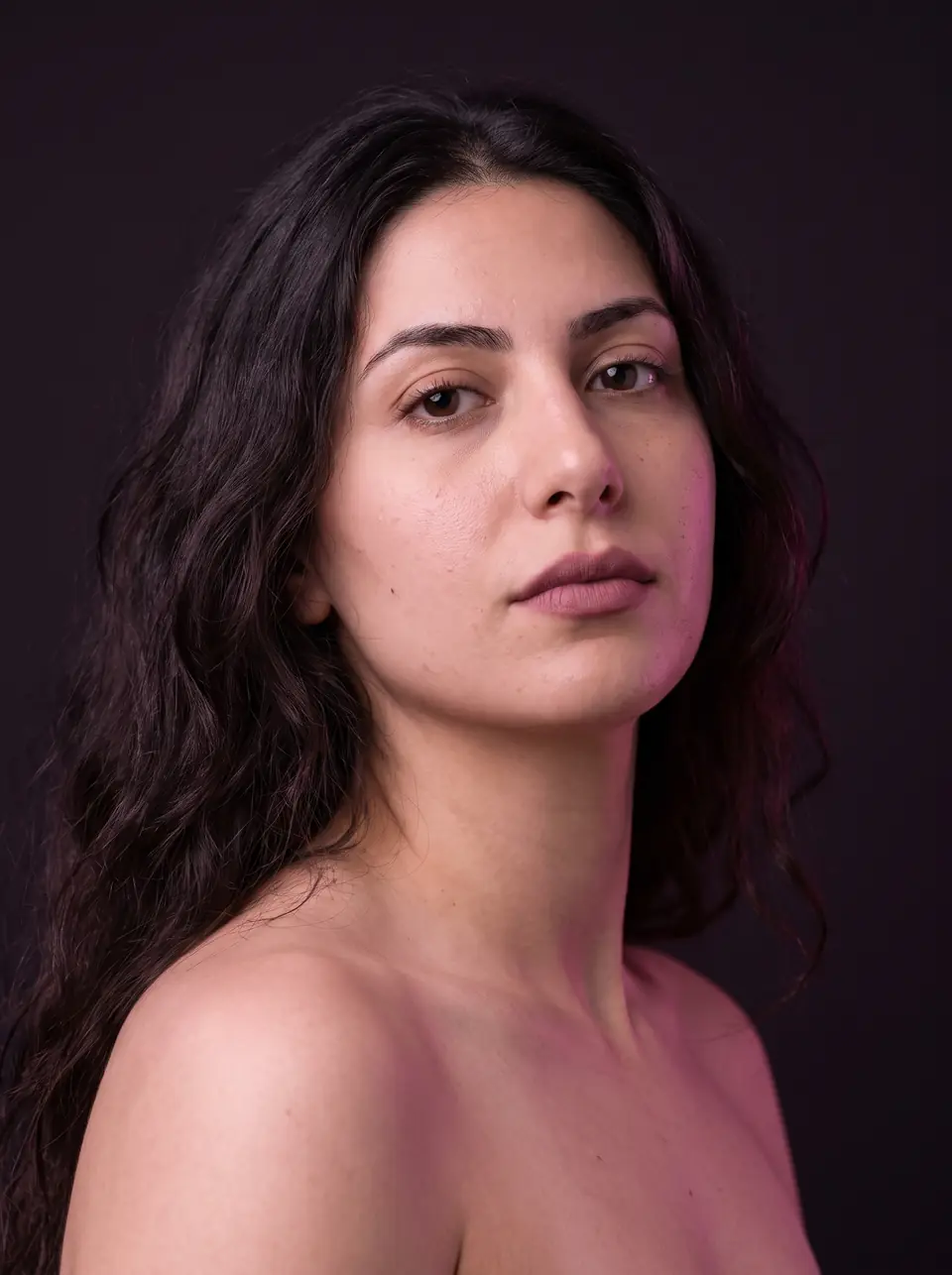 Portrait of a woman with long dark waves and a direct gaze in soft light